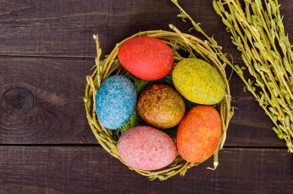 Farverige malede æg i en rede af kviste af pil på en mørk træbaggrund. Traditionelt til påske. Den øverste visning - Stock-foto