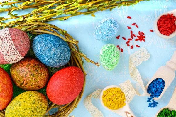 Farverige malede æg i en rede af kviste af pil på en lys baggrund og flerfarvet ris til dekorativt maleri. Traditionelt til påske. Den øverste visning - Stock-foto