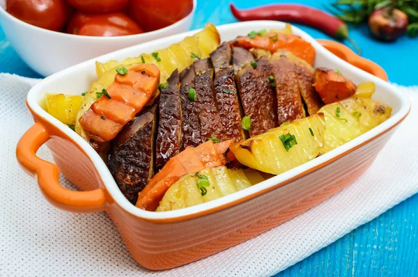 Roasted fillet of brisket goose, sliced, potatoes rustic in a ceramic bowl with marinated tomatoes on a blue wooden background.