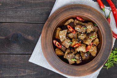 Koyu ahşap arka plan üzerinde bir kil kase biber soslu kızarmış domuz eti parçaları. Üstten Görünüm