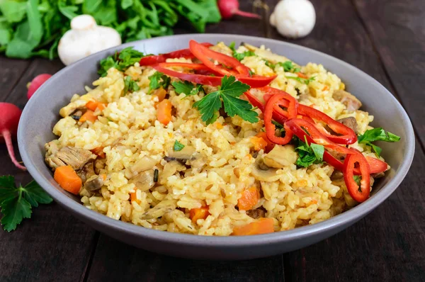 El plato tradicional asiático - pilaf con la carne, las setas y el pimiento capi en la escudilla sobre el fondo oscuro de madera . — Foto de Stock