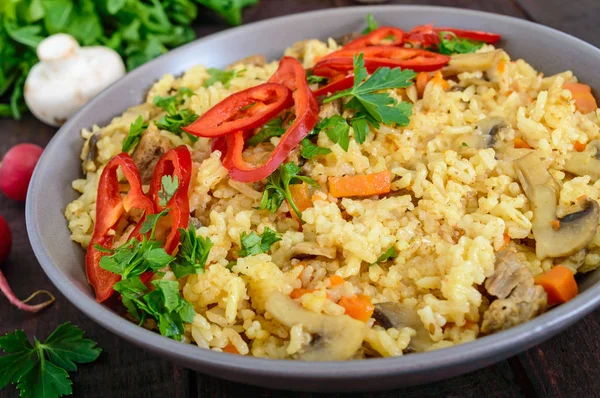 El plato tradicional asiático - pilaf con la carne, las setas y el pimiento capi en la escudilla sobre el fondo oscuro de madera . — Foto de Stock