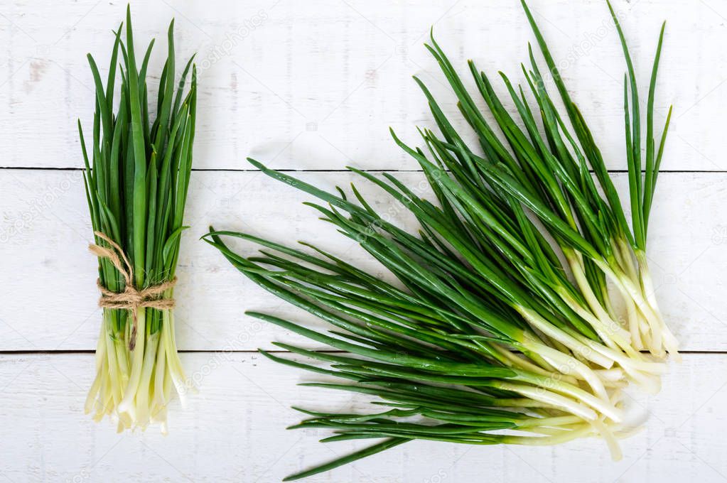 Young feathers (leaves) of a green onion on a white wooden background, collected in a bundle and scattered. The top view. The first spring greens. Ingredient for salads.