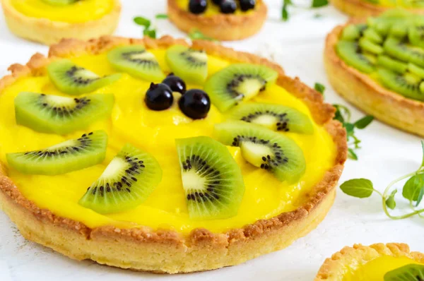 Tartlets, tartas de creme, kiwi e groselha preta sobre um fundo de madeira branca . — Fotografia de Stock