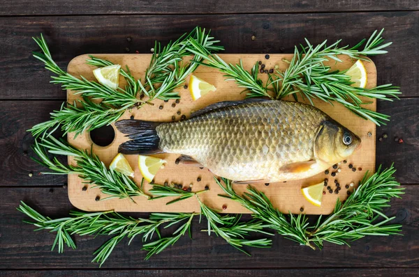 Groot woon carp (crucian) op een snijplank met rozemarijn takken. Verse vangst. Bovenaanzicht. — Stockfoto