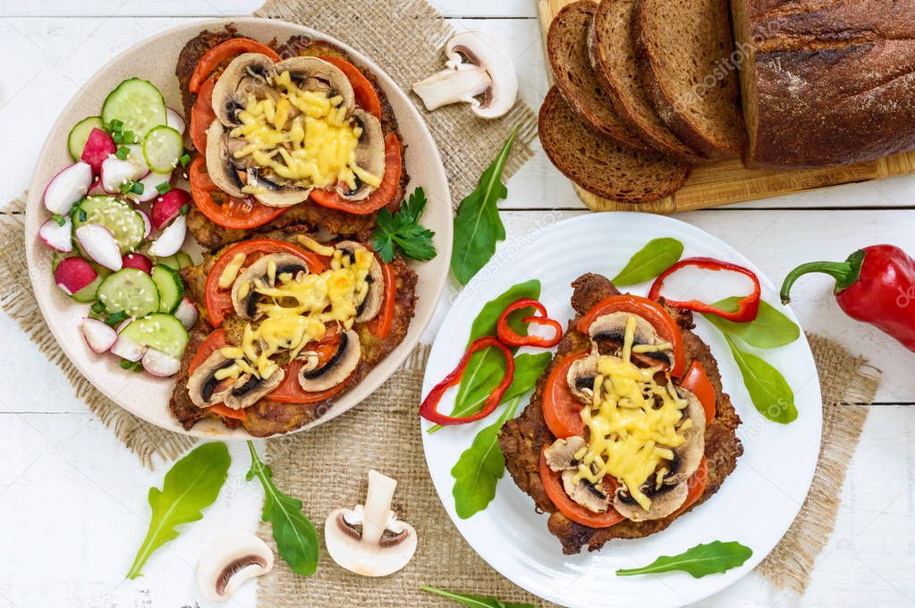Chops baked with mushrooms, tomatoes and cheese on a white wooden background. Meat 