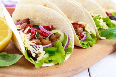 Taco geleneksel Meksika yemeği var. Tortilla doldurulmuş tavuk, çan ve sıcak biber, fasulye, marul, peynir, Beyaz ahşap zemin üzerinde salsa sos ile mavi soğan ile. Yakın çekim