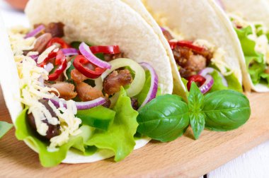 Taco geleneksel Meksika yemeği var. Tortilla doldurulmuş tavuk, çan ve sıcak biber, fasulye, marul, peynir, Beyaz ahşap zemin üzerinde salsa sos ile mavi soğan ile. Yakın çekim