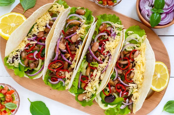 Tacos este un fel de mâncare tradițional mexican. Tortilla umplute cu pui, clopot și ardei iute, fasole, salată verde, brânză, ceapă albastră cu sos de salsa pe fundal alb din lemn . — Fotografie, imagine de stoc