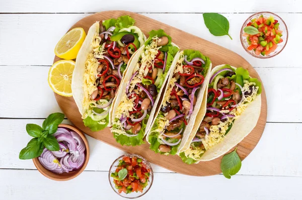 Tacos este un fel de mâncare tradițional mexican. Tortilla umplute cu pui, clopot și ardei iute, fasole, salată verde, brânză, ceapă albastră cu sos de salsa pe fundal alb din lemn. Privire de sus . — Fotografie, imagine de stoc