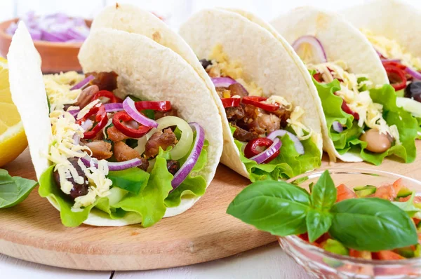 Tacos adalah hidangan tradisional Meksiko. Tortilla diisi dengan ayam, lonceng dan paprika panas, kacang, selada, keju, bawang biru dengan saus salsa di latar belakang kayu putih . — Stok Foto