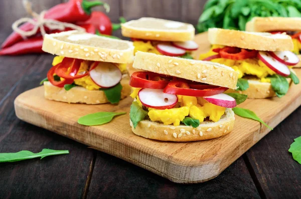 Sandwich con huevos revueltos, rúcula, rábano, pimentón kapi y semillas de lino sobre una tabla de cortar sobre un fondo de madera oscura. Desayuno rápido y sabroso . — Foto de stock gratis