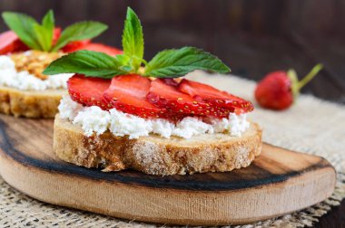 Küçük bir bruschetta lor ve koyu ahşap arka plan üzerinde taze çilek ile. 