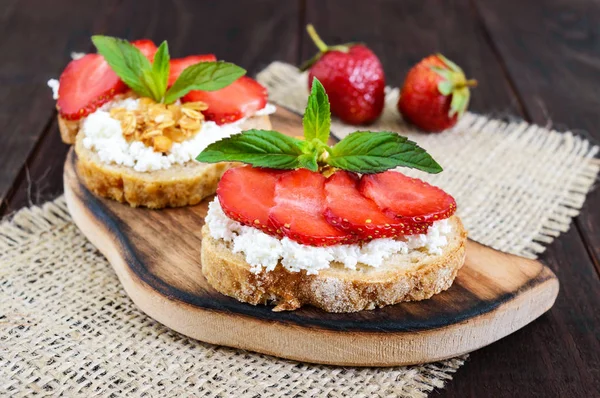 Una pequeña bruschetta con cuajada y fresas frescas sobre un fondo de madera oscura . —  Fotos de Stock