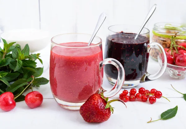 Beeren-Smoothie in Glasbechern, Joghurt, Müsli, frische Beeren auf weißem Holzhintergrund. — Stockfoto