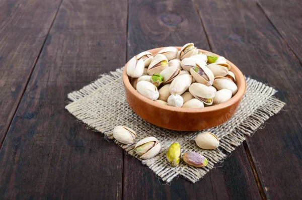 Useful nuts - pistachios in a ceramic bowl on a dark wooden background. — Stock Photo, Image