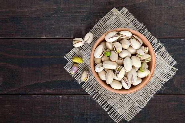 Användbar nötter - pistagenötter i en keramikskål på en mörk trä bakgrund. — Stockfoto