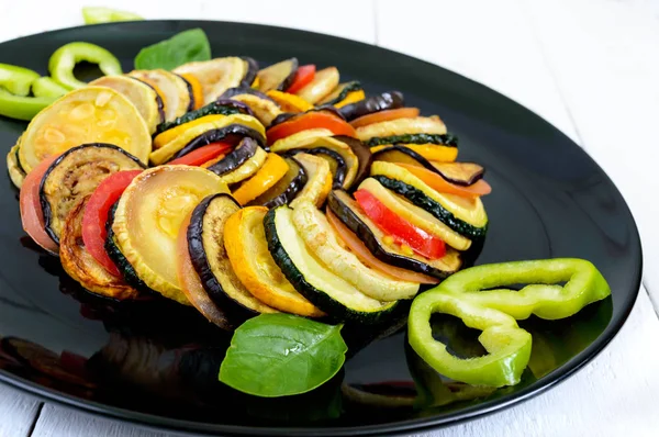 Beyaz bir arka plan üzerinde siyah bir tabak kızarmış kabak dilimleri, patlıcan, domates. Ratatouille. — Stok fotoğraf