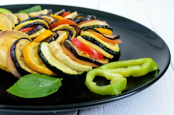 Fette di zucchine fritte, melanzane, pomodoro su un piatto nero su fondo bianco. Ratatouille . — Foto Stock