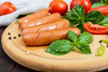 Domates ve fesleğen yuvarlak kesme tahtası koyu ahşap arka plan üzerinde sulu sosis.