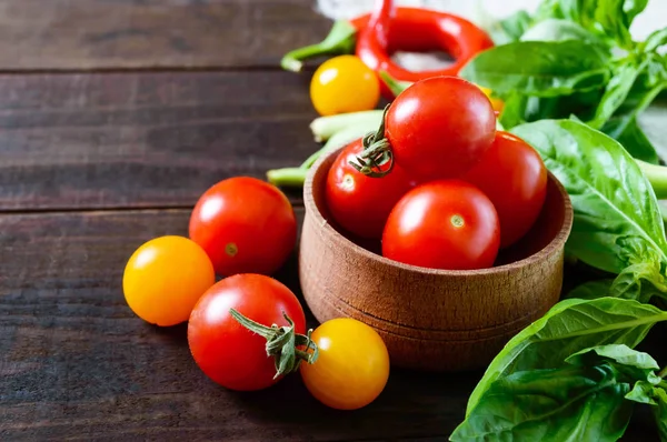 Kırmızı ve sarı kiraz domates fesleğen yaprakları koyu ahşap arka plan üzerinde arasında.