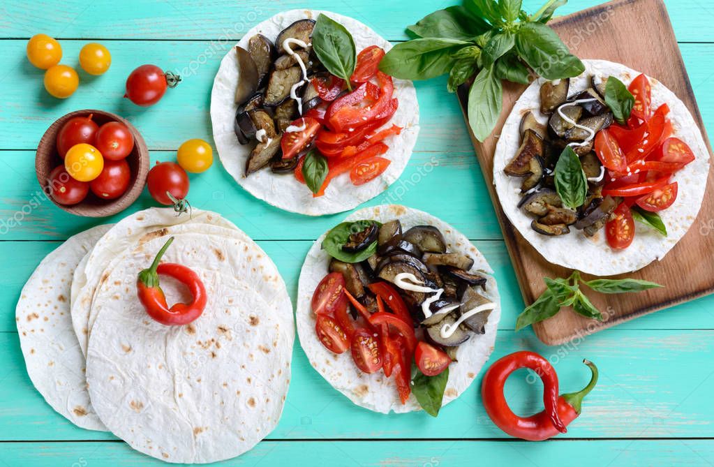 Vegetarian tacos with eggplant, cherry tomatoes, sweet peppers on a bright wooden background. Mexican snack.