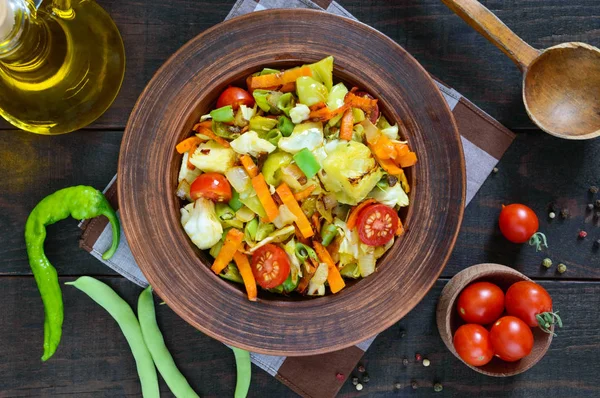 Lahana, yeşil fasulye, havuç, domates, soğan, koyu ahşap arka plan üzerinde bir kil kase içinde tatlı biber, sebze güveç. Sıcak salata. Vejetaryen mutfağı