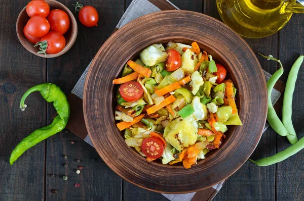 Lahana, yeşil fasulye, havuç, domates, soğan, koyu ahşap arka plan üzerinde bir kil kase içinde tatlı biber, sebze güveç. Sıcak salata. Vejetaryen mutfağı