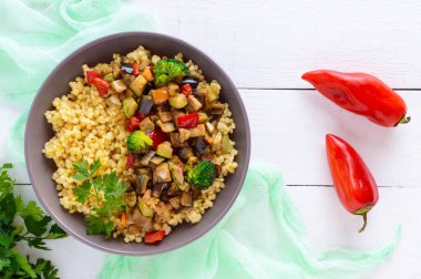 Sıcak vejetaryen kuskus ve kızarmış sebze (patlıcan, kabak, soğan, tatlı biber, brokoli) Beyaz ahşap zemin üzerinde seramik bir kasede salatası. Doğru beslenme. Üstten Görünüm.