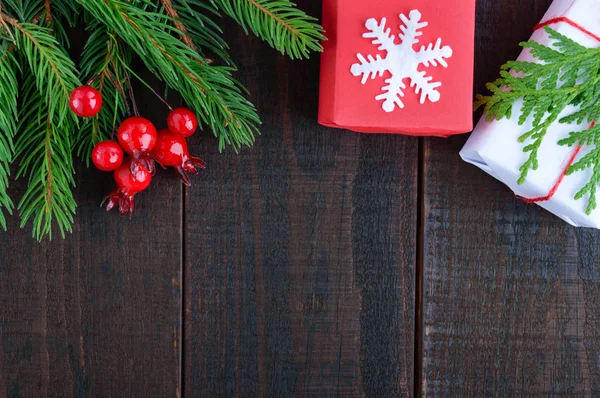 Новый год, рождественская тема. Подарочные коробки, зеленые еловые ветви, ягоды на темном деревянном фоне. Праздничный фон . — стоковое фото