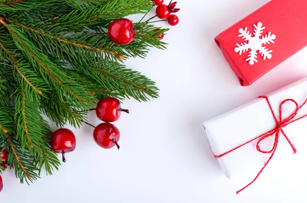 Зеленые еловые ветви украшены ягодами и подарочными коробками на белом фоне. Новый год, рождественский декор — стоковое фото