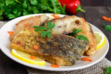 Limon ve koyu ahşap arka plan üzerinde bir tabakta yeşillik ile kavrulmuş sazan parçaları.