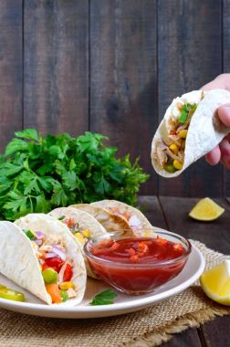 Taco - buğday tortilla et, sebze, yeşillik ve domates ile Mısır ile koyu ahşap arka plan üzerinde sos. Geleneksel Meksika mutfağı. Atıştıracak bir şeyler el tutar.