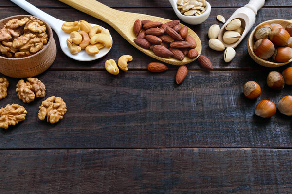 Assorted different nuts, prunes, pumpkin seeds in spoons on a dark wooden background.