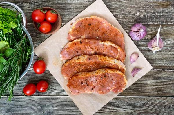 Fresh and raw meat. Sirloin steaks in a row ready to cook. Large pieces of raw meat in marinade with spices on paper on a wooden table.Top view.