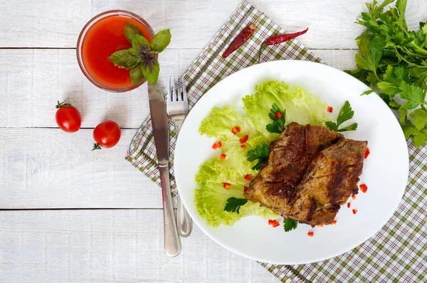 Kızarmış domuz kaburga yeşillik ve domates suyu Beyaz ahşap zemin üzerinde bir plaka üzerinde.