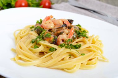 Makarna tagliatelle deniz ürünleri ve ahşap bir masa üzerinde beyaz bir plaka üzerinde krema sos ile.