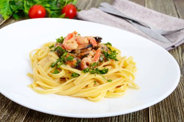 Makarna tagliatelle deniz ürünleri ve ahşap bir masa üzerinde beyaz bir plaka üzerinde krema sos ile.