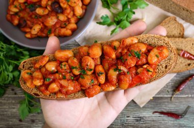 El bir dilim çavdar ekmek fasulye ile tablo arka planda tutar. Otlar ve baharatlar ile domates sosu haşlanmış fasulye. Üstten Görünüm. Paskalya menü. Vegan yemek.