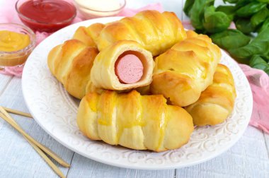 Sosisli farklı sos ile beyaz ahşap zemin üzerinde seramik plaka üzerinde yumuşak ev yapımı çörekler. Hamur sosis.