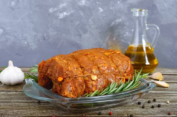 A large piece of pork meat on a wooden table, marinated in spices, stuffed with garlic and carrots, ready for baking. Preparation of a festive meat dish.