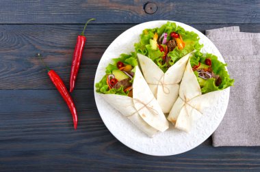 Burrito kıyılmış et, avokado, sebze, koyu ahşap arka plan üzerinde bir tabakta acı biber ile. Doldurulmuş tortilla. Geleneksel Meksika meze. Üstten Görünüm.