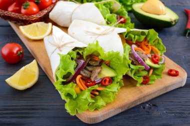 Burrito kıyılmış et, avokado, sebze, koyu ahşap arka plan üzerinde bir kesme tahtası üzerinde acı biber ile. Doldurulmuş tortilla. Geleneksel Meksika meze.