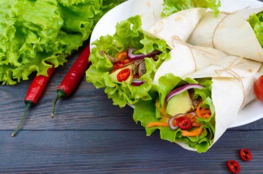 Burrito kıyılmış et, avokado, sebze, koyu ahşap arka plan üzerinde bir tabakta acı biber ile. Doldurulmuş tortilla. Geleneksel Meksika meze.