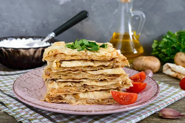 Pie, casserole pita with mushrooms, cottage cheese and cheese on a plate on a wooden background. Layer Cake.