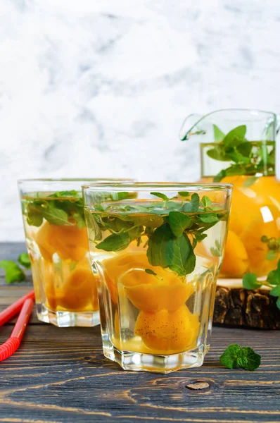 Summer cold drinks. Delicious refreshing drink with apricot and mint in glasses on a wooden table. Compote of fruits. Selective focus.