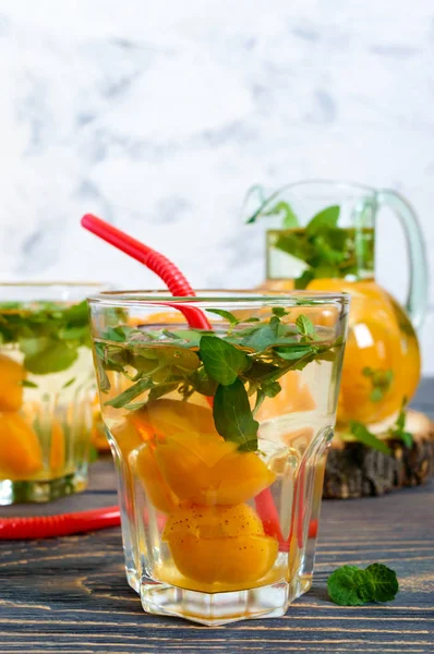 Summer cold drinks. Delicious refreshing drink with apricot and mint in glasses on a wooden table. Compote of fruits. Selective focus.