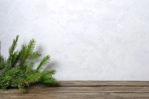 Wooden table near a light concrete wall with green spruce branches in the corner. Photo background. Copy space. Christmas, New Year theme.