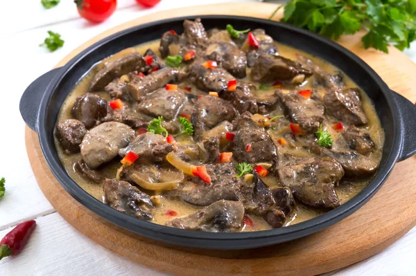 Turkey liver with onions and mushrooms in a creamy sauce on a white wooden background. Diet menu