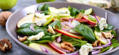 Ispanaklı, elmalı, kırmızı soğanlı, mavi peynirli, fındıklı lezzetli diyet fitness salatası. Düzgün beslenme. Hafif beton arkaplan